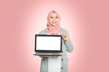 portrait of beautiful Muslim woman wearing hijab showing off digital computer laptop. teenage girl using laptop, isolated on pink background.