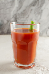 One transparent glass cup with red tomato juice and a sprig of celery on a light background. Healthy food concept. Vertical orientation. Selective focus.