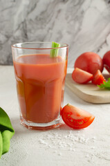 One transparent glass cup with red tomato juice and a sprig of celery on a light background. Healthy food concept. Vertical orientation. Selective focus.