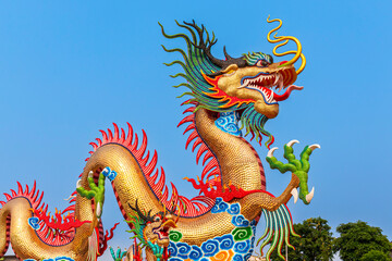 Fototapeta premium Golden Chinese dragon statue with a blue sky in the background.