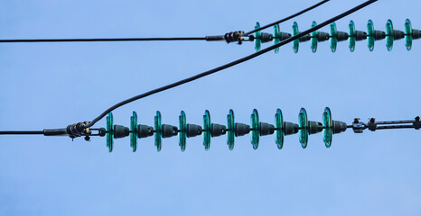 Close up of a transparent turquoise high voltage insulator or isolator in sunlight on electric tower on blue sky background. Electric power transmission line