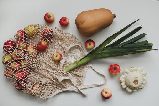 autumn harvest with sqush, pumpkin, apples and vegetables in a mesh shopping bag on white background