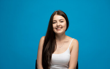 Human emotions. Happy, smiley and positive brunette girl in a white t-shirt looking at camera, smiling carefree on blue background studio.