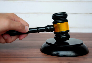 Hand holding lawyer gavel on wooden table background.