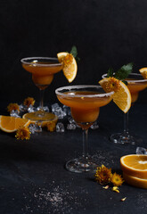 Glasses of orange cocktail decorated with orange and sugar on the edge of glass on black background