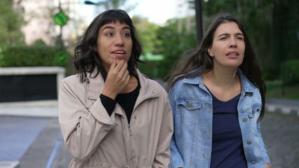 Two girlfriends walking outside gossiping together. Female friends in conversation on a walk