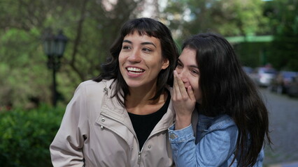 Two female friends gossiping while walking outside in street. Young women conversation on sidewalk