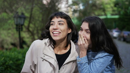 Two female friends gossiping while walking outside in street. Young women conversation on sidewalk