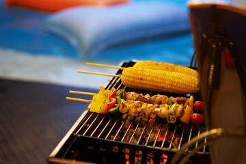 corn and barbecue sticks on stove on blur swimming pool background party