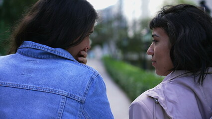 Female friends gossiping outside while walking together. Back of two people talking outdoors