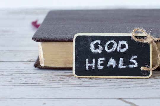 God heals, a handwritten text written with chalk on a small blackboard with a closed Holy Bible Book in the background. Christian biblical concept of restoration, healing, and salvation. A closeup.