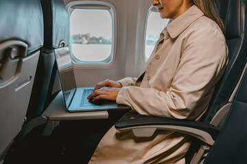 Close up of woman passenger sitting in the airplane and working laptop during flight