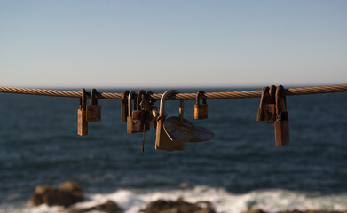 Rusted locks and an iron heart on a steel cable against the background of the blue sea - 520056179