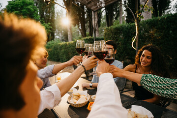 Group of friends outside eat and have fun together toasting with red wine glasses at sunset at the hotel restaurant where are staying - Cheerful people laugh and joke evening  - Party at home - 520056307