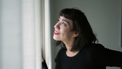 One beautiful hispanic girl looking out through curtain window checking sunlight day