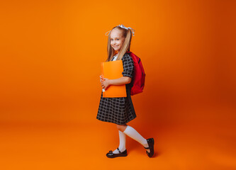 Back to school. A schoolgirl with a school bag on an isolated yellow studio background. a little girl holds a folder and a backpack.