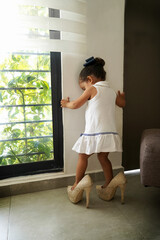 Niña feliz y traviesa con los zapatos tacones de su mamá jugando a ser grande, divertida posando y haciendo travesuras