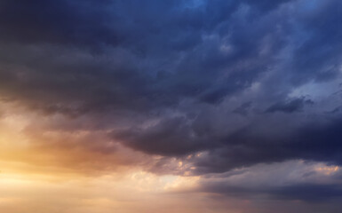 Naklejka na ściany i meble Dramatic sunset sky with dark rainy clouds and bright sunshine.