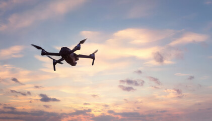 Close up of professional remote control drone flying against dramatic sunset sky background.