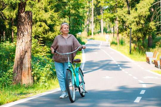 Senior older elderly modern woman rides a bicycle in a city park in the forest. Active pensioner, health lifestyle