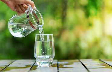 Obraz premium Pour clean water from a jug into a glass placed on a wooden bar. 