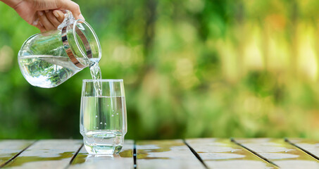 Pour clean water from a jug into a glass placed on a wooden bar.	

