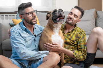 Happy gay couple sitting on floor and playing with dog at home. High quality photography