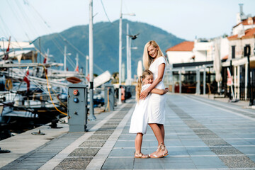 Smiling caucasian blonde  mother and daugher walking by harbor with yachts on a touristic sea resort