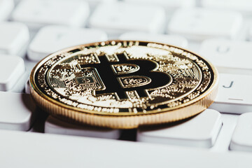 One gold Bitcoin token laying on a white computer keyboard