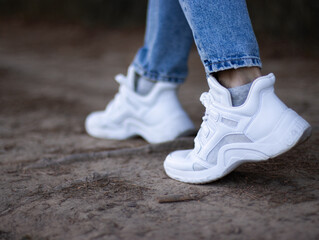 Fototapeta na wymiar Fashionable white sneakers on female legs, close-up.