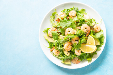 Shrimp salad with arugula and avocado at blue table. Top view with space for text.