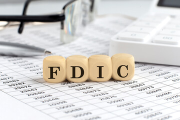 wooden cubes with the word FDIC on a financial background with chart, calculator, pen and glasses, business concept.