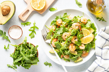 Green shrimp salad with arugula and avocado at white table. Top view image.
