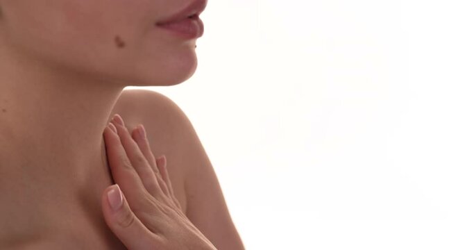 Side view of a caucasian woman gently applying moisturiser cream on her collarbone and neck. Isolated on a white background.