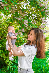Obraz premium Young beautiful mother and cute 3-month-old baby in lilac bushes in summer