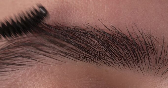 Macro of a woman brushing her eyebrow with an eyebrow brush.