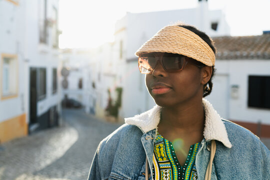 Black woman with hat and sunglasses looking away on the street