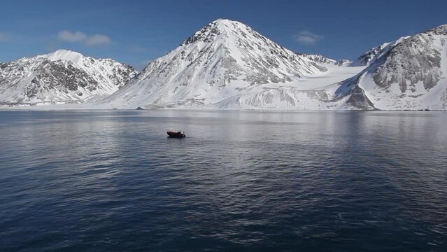 Lancha parada en un mar en calma bajo un cielo azul y monta&ntilde;as nevadas en el archipi&eacute;lago de Spitsbergen, islas Svalbard en noruego