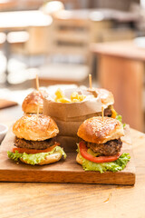 Four hamburgers on a wooden board and french fries served in a wooden paper basket