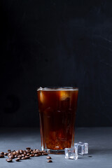 cup of coffee with beans.Tasty Ice coffee in a tall glass. Cold drink with coffee beans and ice on the black table. Cold summer drink on the black background with copy space. vertical