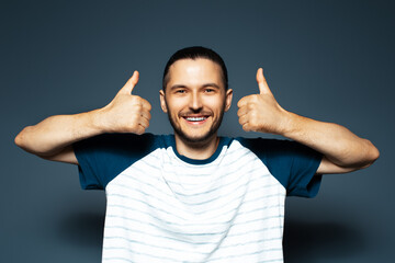 Fototapeta premium Studio portrait of young man showing thumbs up on background of blue color.