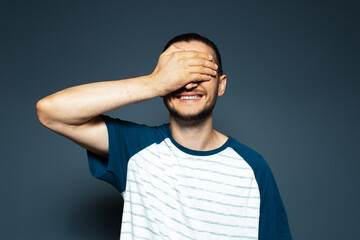 Studio portrait of young smiling man holding palm on face on  blue background.