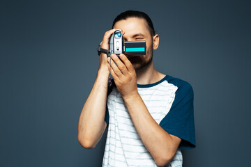 Studio portrait of young guy with digital video camera in hands. Making movie.