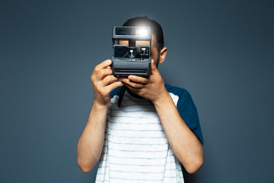 Studio portrait of young man photographer making photo with polaroid camera.