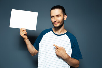 Studio portrait of guy point finger on white empty paper board. Blue background.