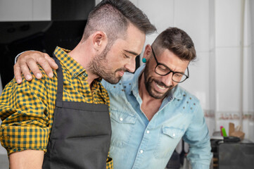 Happy hipster gay couple in love standing in the kitchen. They are cooking dinner together at home. High quality photography