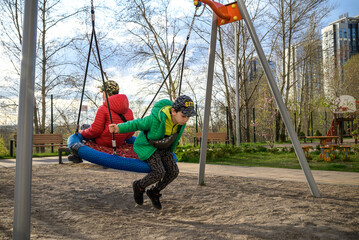 Two little kid boys having fun with swing on outdoor playground. Children, best friends and siblings swinging on warm sunny spring or autumn day. Active leisure with kids. Casual boy fashion