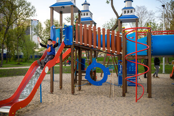 Fototapeta na wymiar Portrait of cute boy playing on slide at playground on sunny morning