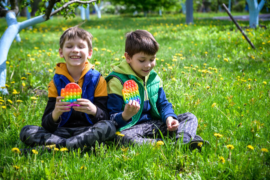 children playing with colorful toys Pop It. Boys on vacation. Tired of games, relaxing on the grass. Summer time for children, two boys friends at reboot together