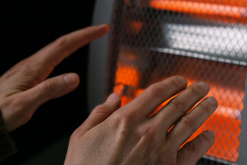 Close-up of hands reaching for the portable quartz heater. Selective focus